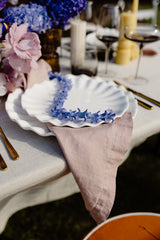 Decorative table setting with a shell-shaped plate, lavender napkin, and floral arrangement.