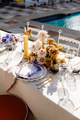 Decorative table setting with linen napkins and tablecloths, flowers and candles by a poolside.