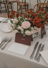 Table setting with linen napkins and tablecloths, floral centerpieces, silverware, and place cards.