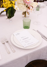 Table setting with white tablecloth, green glass, and floral decorations.