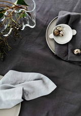 Cool grey and graphite grey linen napkins on a grey tablecloth with green foliage and minature spotted eggs.
