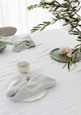 Mint linen napkins on white tablecloth with mushrooms and leafy green branches hanging overhead.