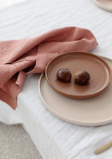 Rose linen napkins on white tablecloth alongside ceramic plates and chestnuts.