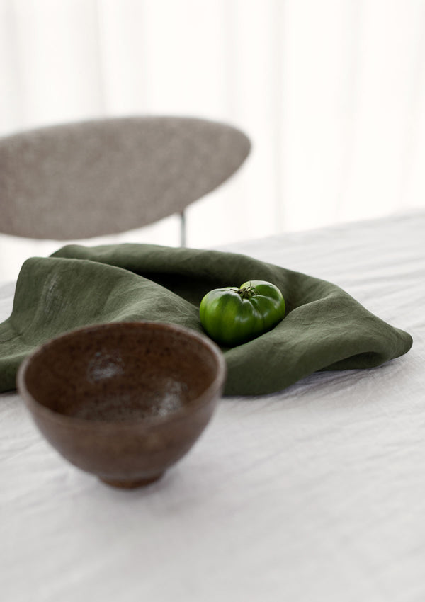 Forest green linen napkin on a whote tablecloth with a green capsicum and wooden bowl.